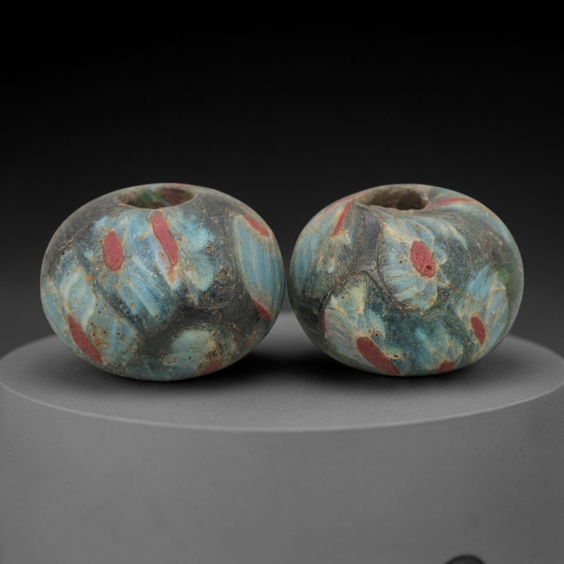 A Pair of Venetian Millefiori Glass Beads, 19th-20th Century, 80AD: Crafted from translucent turquoise glass with dark inclusions, each bead is formed as a sphere with a central drilled perforation. The surface is decorated with characteristic millefiori canes, featur