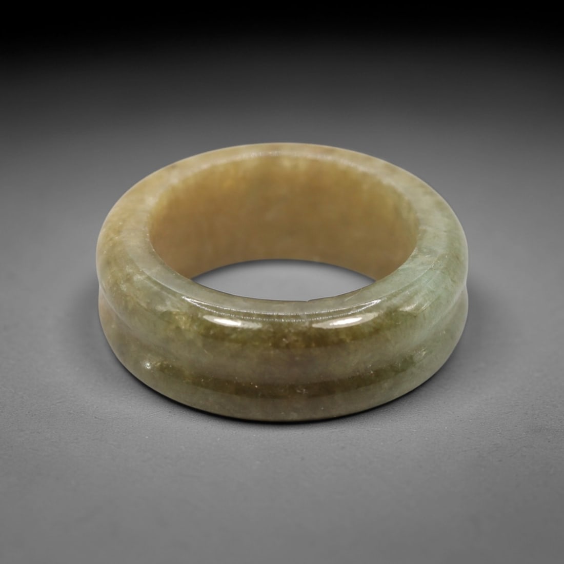 A Chinese Jadeite Jade Ring, 20th Century, 9XN: Carved from greenish jadeite jade, the ring is formed as a thick, circular band with a smooth, highly polished surface. The form features a wide, gently convex outer profile and a concave inner surfac