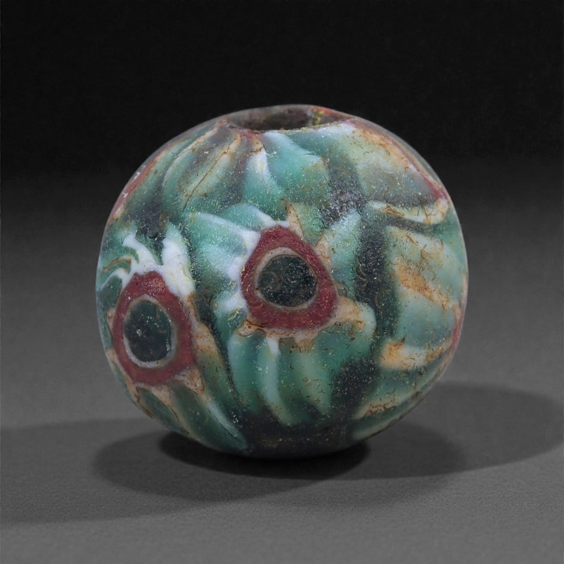 Antique Glass Bead - Venetian Eye Pattern Sphere, 78J: Fashioned in variegated glass with swirling green, white, and amber tones, this small spherical bead displays the characteristic ocular motifs associated with Venetian bead production of the late medi
