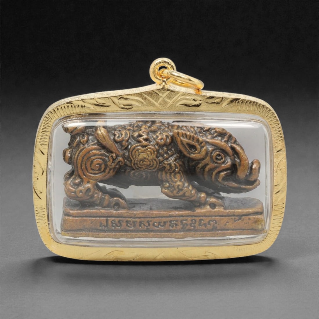 A Thai Mythical Boar Amulet Pendant, 20th Century, 16FP: This rectangular pendant with rounded corners features a copper alloy core, encased in an ornate gilded metal frame with a transparent protective cover, measuring 4.7 x 3.8 cm (1 7/8 x 1 1/2 in.). The
