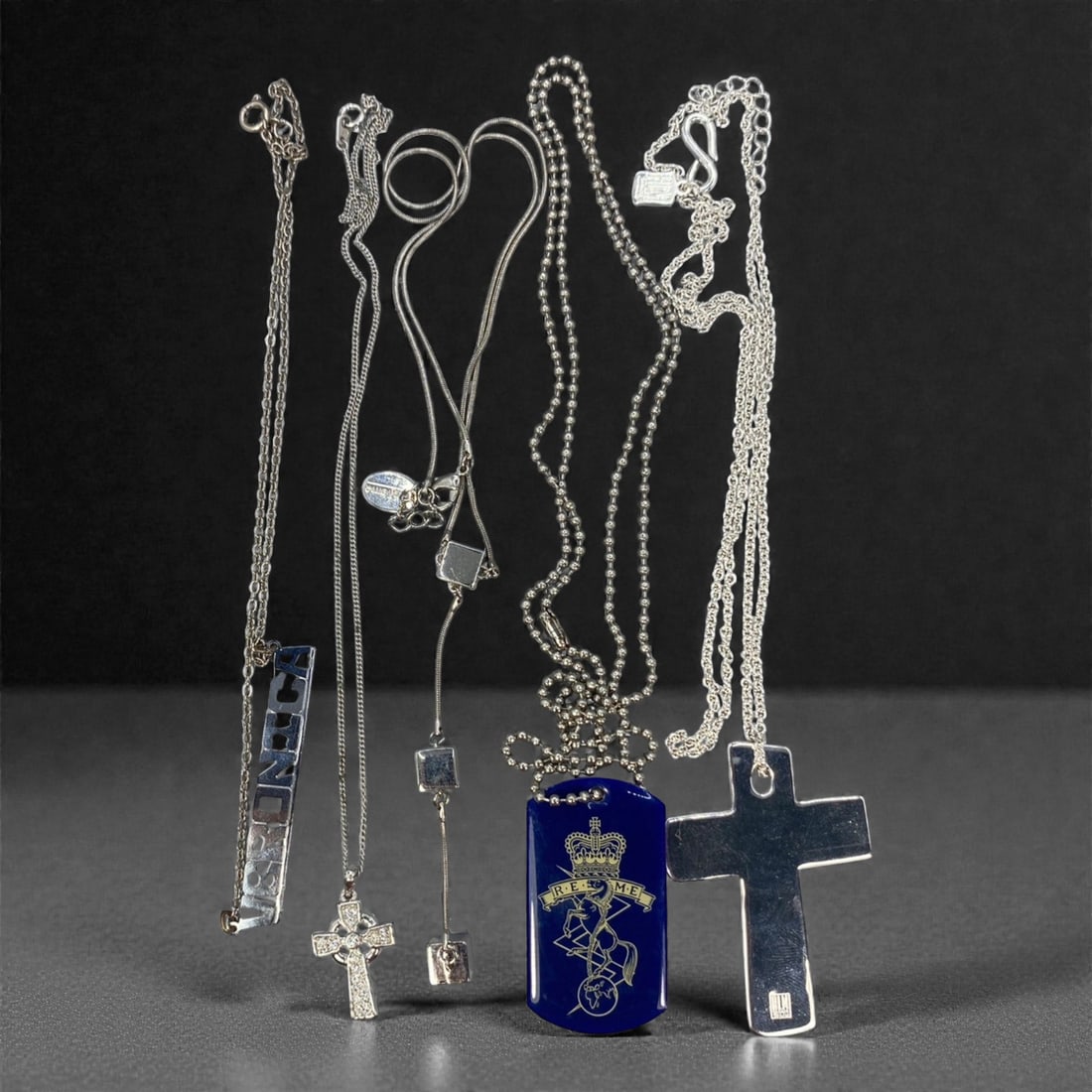 An Estate Lot of Five Pendant Necklaces, Late 20th Century, 73FK: The lot comprises five pendant necklaces, crafted from silver-toned alloy, with crystal, enamel, and glass accents. The pieces include: a cable chain with a rectangular pendant of mirrored, cut-out le