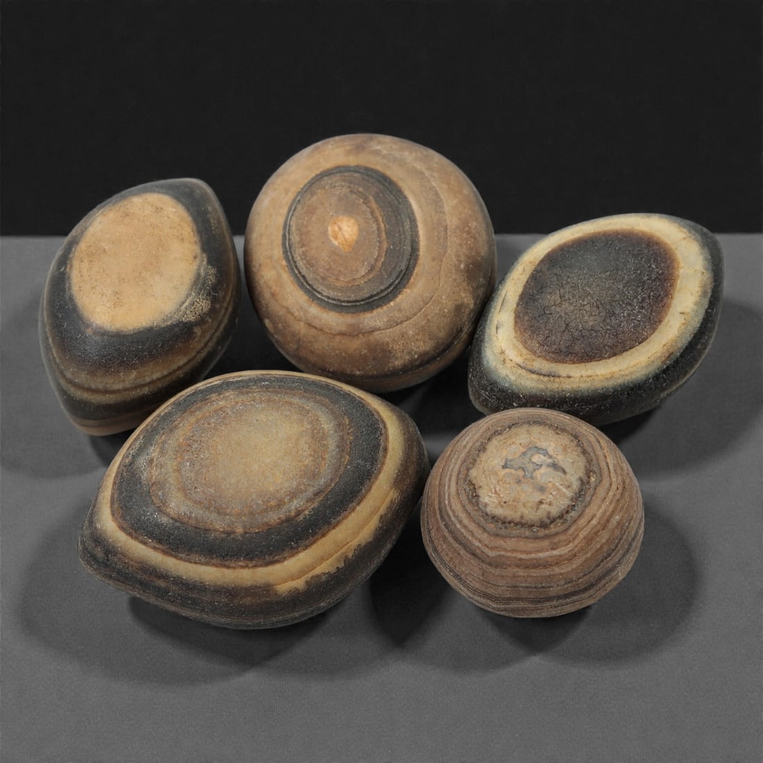 A Group of Tibetan Luk Mik ("Goat's Eye") Agate Beads, 11th-14th Century CE, 40FN: Comprising five pieces, each bead is fashioned from naturally banded agate, showcasing the distinctive luk mik ("goat's eye") formation characterized by concentric, circular layering at the center. Th