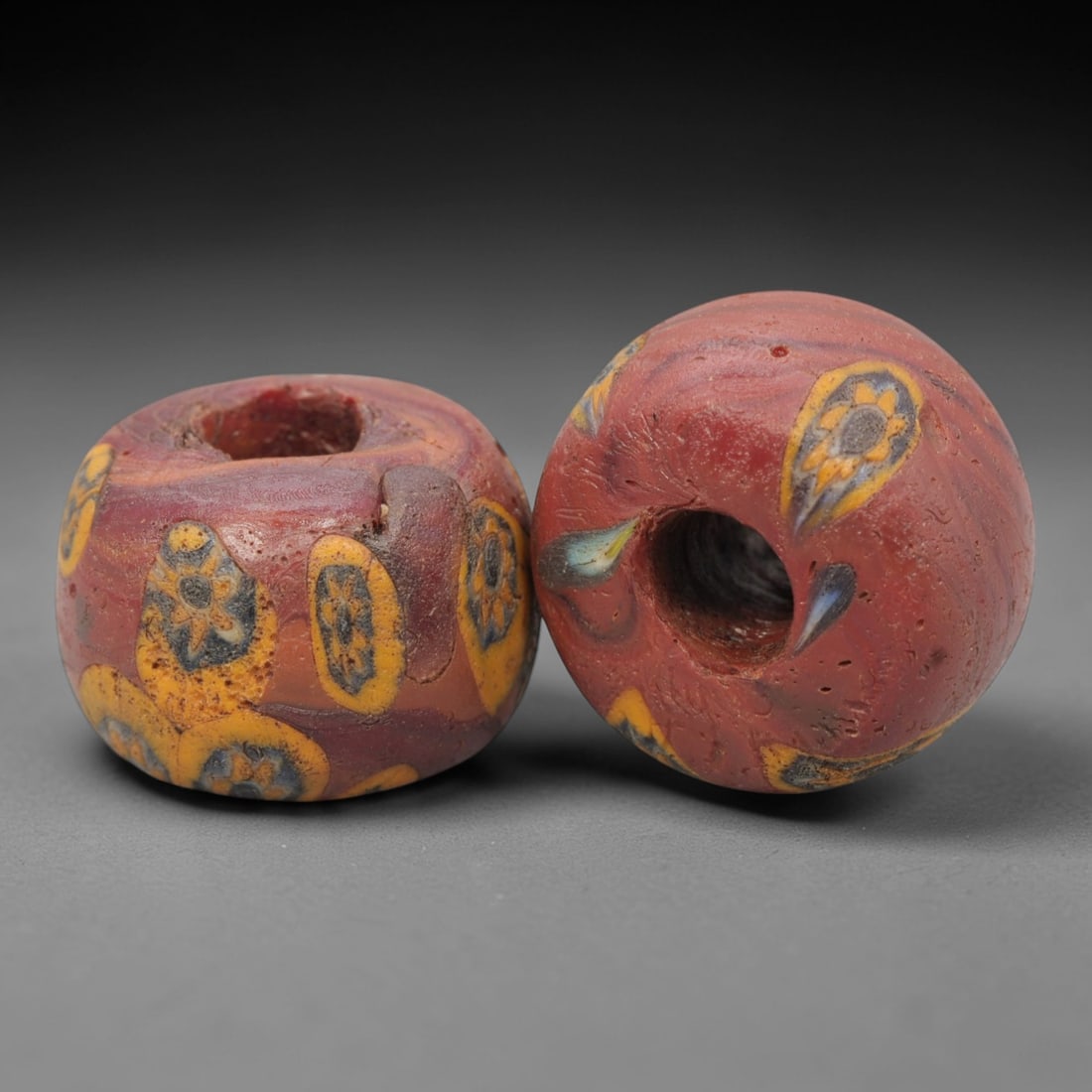 A Pair of Venetian Glass Trade Beads, 19th-20th Century, 20ZM: Formed as barrel-shaped and spherical beads, each is crafted from opaque red glass with a central perforation for suspension. The surface is decorated with multiple polychrome eye motifs, each featuri
