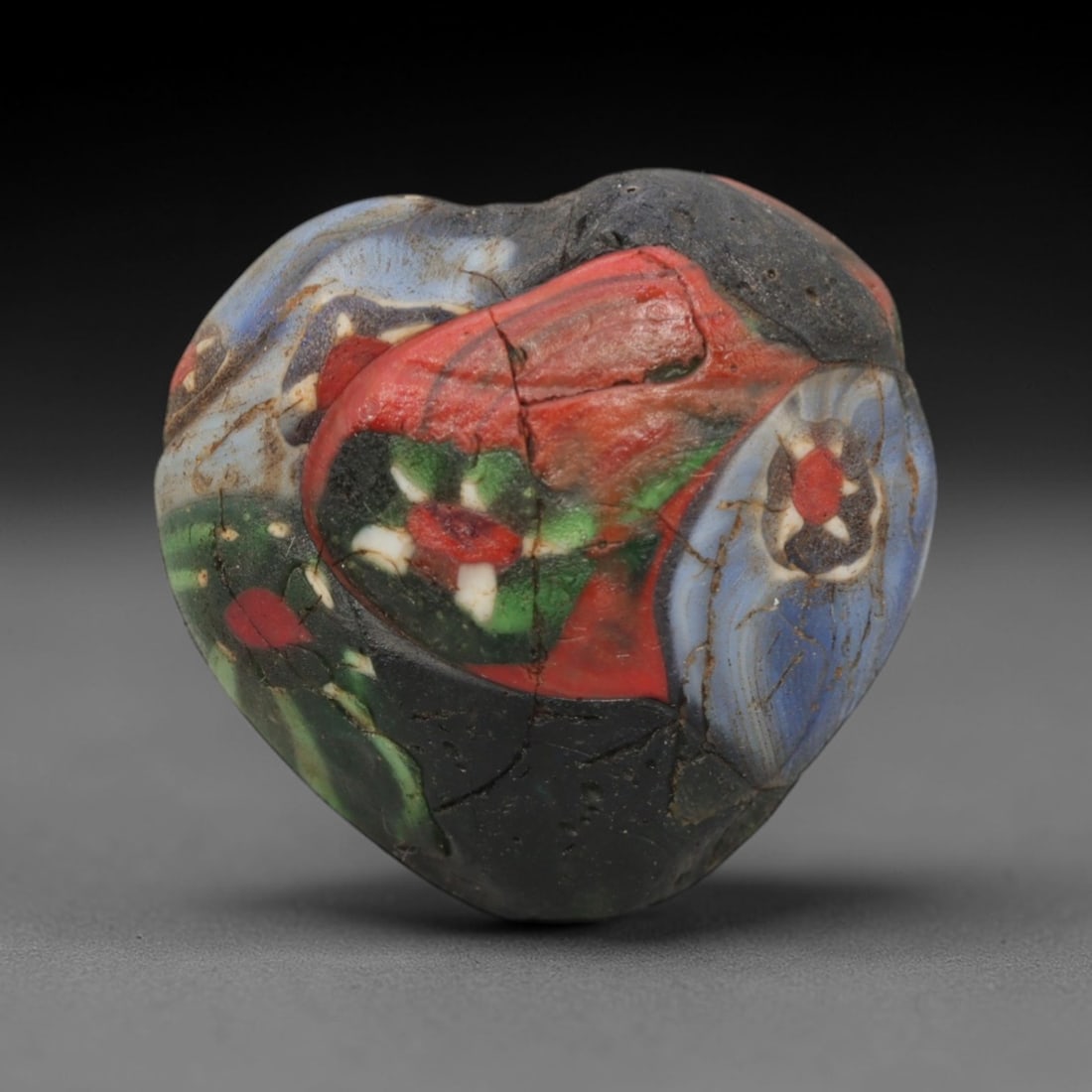 A Venetian Mosaic Heart Bead, 19th-20th Century, 17ZM: Fabricated from opaque and translucent glass, the bead is heart-shaped with a central perforation for suspension. The surface is decorated with large, irregular mosaic inlays in red, green, blue, and