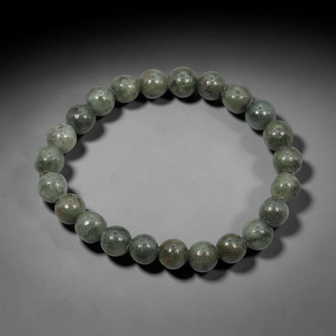 A Chinese Jadeite Jade Bead Bracelet, 20th Century, 56ZK: Composed of a single strand of spherical jadeite jade beads forming a circular bracelet. The beads display natural tonal variation from pale green to deep green, with visible internal mineral inclusio