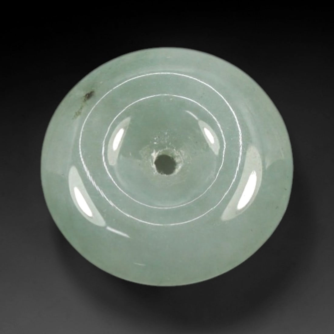 A Chinese Jadeite Jade Bead, 20th Century, 2XN: Carved from pale green jadeite jade with subtle tonal variation and minor natural inclusions, the bead is formed as a spherical object with a smooth, highly polished surface. The form features a centr