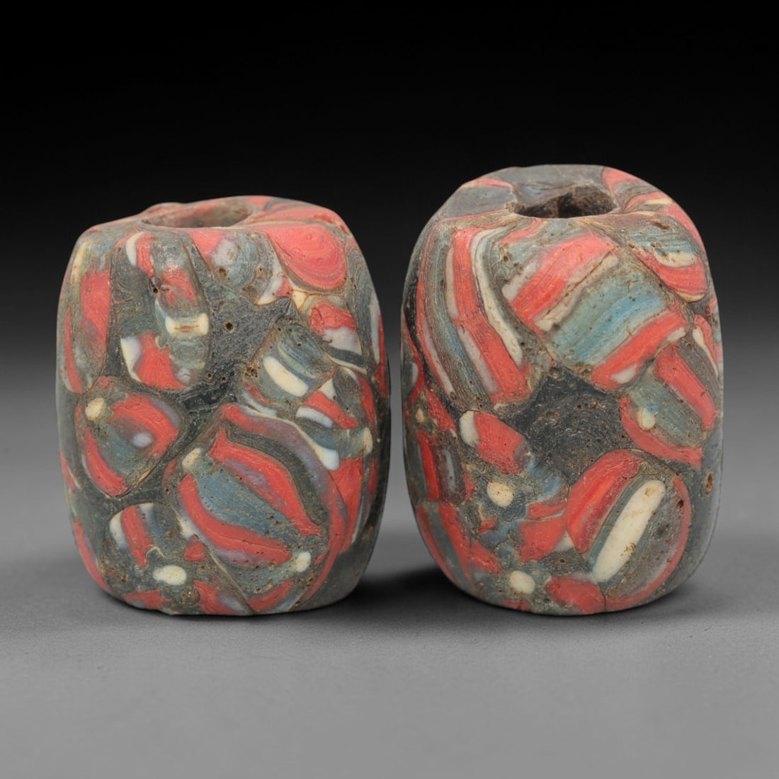 A Pair of Venetian Marbled Glass Beads, 19th-20th Century, 46AD: Fabricated from opaque dark glass, each bead is formed as a short cylinder with a central drilled perforation. The surface displays marbled swirled patterns in red, blue, white, and dark tones, with t