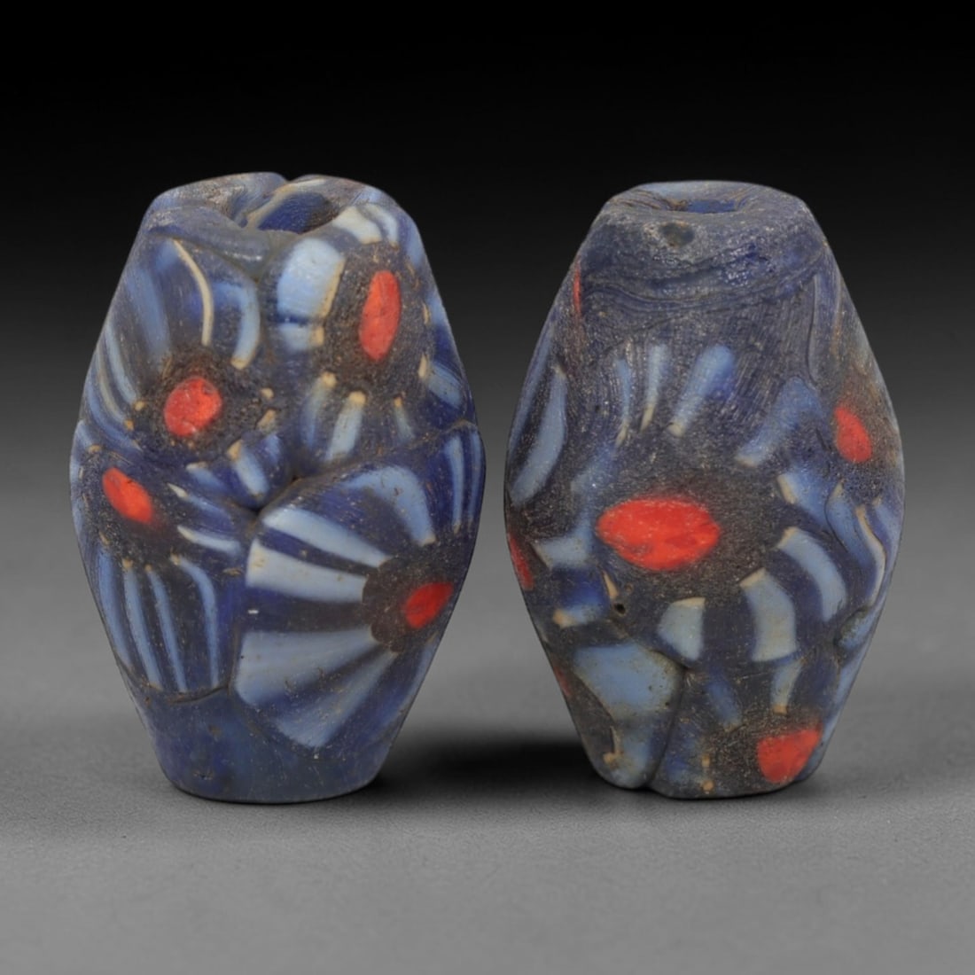 A Pair of Venetian Millefiori Glass Beads, 19th-20th Century, 41AD: Fabricated from opaque dark blue glass, each bead is formed as an elongated bicone with a central drilled perforation. The surface is decorated with characteristic millefiori canes, featuring floral a