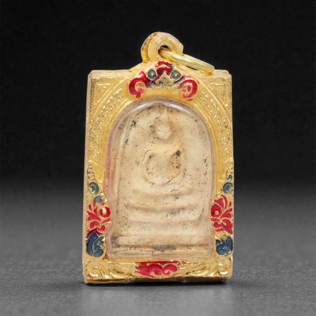 A Thai Phra Somdej Amulet Pendant, 20th Century, 9FP: This rectangular amulet pendant features a traditional Phra Somdej core encased in an ornate gilded metal frame with a transparent protective cover, measuring 5.1 x 3 cm (2 x 1 3/16 in.). The obverse
