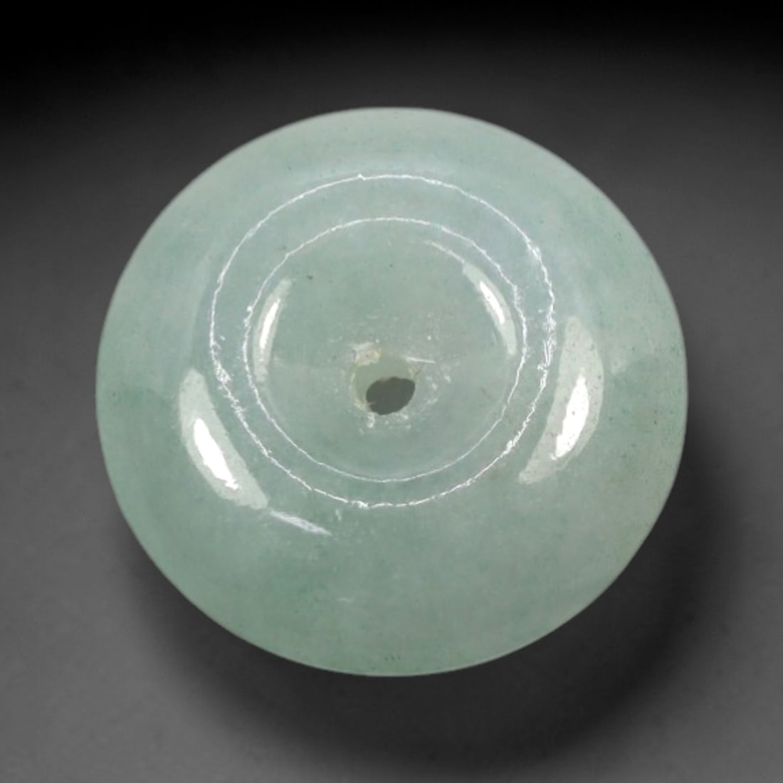 A Chinese Jadeite Jade Bead, 20th Century, 100XM: Carved from pale green jadeite jade with subtle tonal variation and minor natural inclusions, the bead is formed as a spherical object with a smooth, highly polished surface. The form features a centr