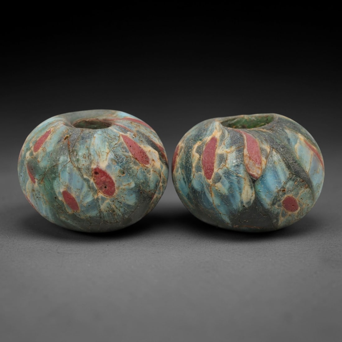 A Pair of Venetian Glass Trade Beads, 19th-20th Century, 65ZM: Formed as spherical beads, each is crafted from translucent glass with a central perforation for suspension. The surface displays embedded, fragmented inclusions of opaque red glass, arranged in abstr