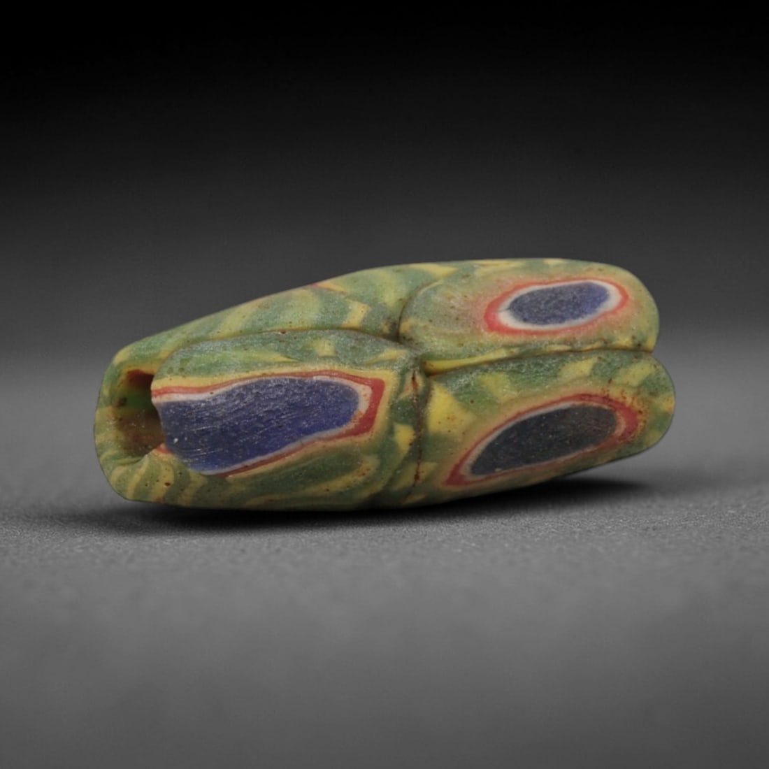A Sino-Himalayan Glass Eye Bead, 18th-19th Century, 32ZN: Formed from translucent green glass with swirling yellow and pale green filamentary inclusions characteristic of mosaic glass working, the bead is barrel-shaped with a central perforation for suspensi