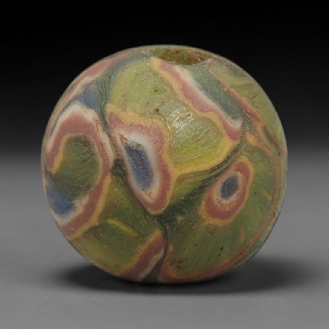 A Sino-Himalayan Glass Eye Bead, 18th-19th Century, 35ZN: Formed from translucent green glass with swirling yellow and pale green filamentary inclusions characteristic of mosaic glass working, the bead is spherical with a central perforation for suspension.
