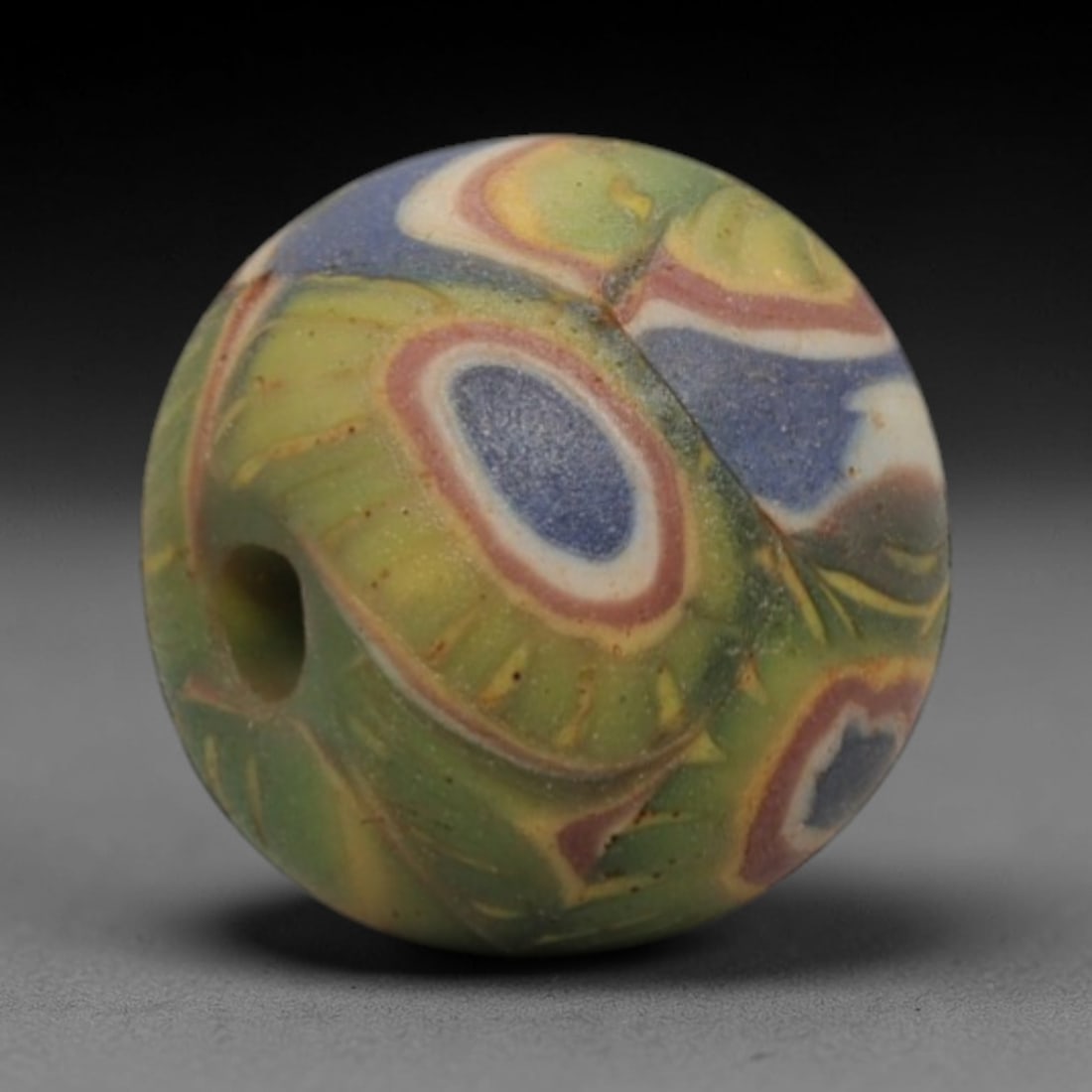 A Sino-Himalayan Glass Eye Bead, 18th-19th Century, 26ZN: Formed from translucent green glass with striking swirling yellow and deep blue filamentary inclusions characteristic of mosaic glass working, the bead is spherical with a well-defined central perfora