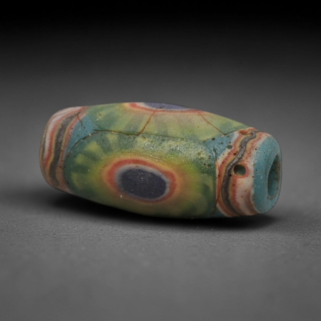 A Sino-Himalayan Glass Eye Bead, 18th-19th Century, 31ZN: Formed from translucent blue-green glass with swirling yellow and pale green filamentary inclusions characteristic of mosaic glass working, the bead is barrel-shaped with a central perforation for sus