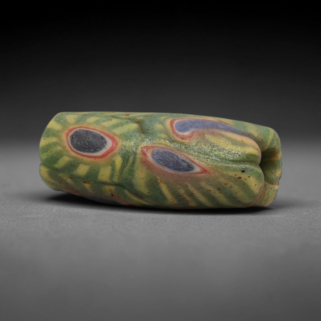 A Sino-Himalayan Glass Eye Bead, 18th-19th Century, 30ZN: Formed from translucent green glass with swirling yellow and pale green filamentary inclusions characteristic of mosaic glass working, the bead is barrel-shaped with a central perforation for suspensi