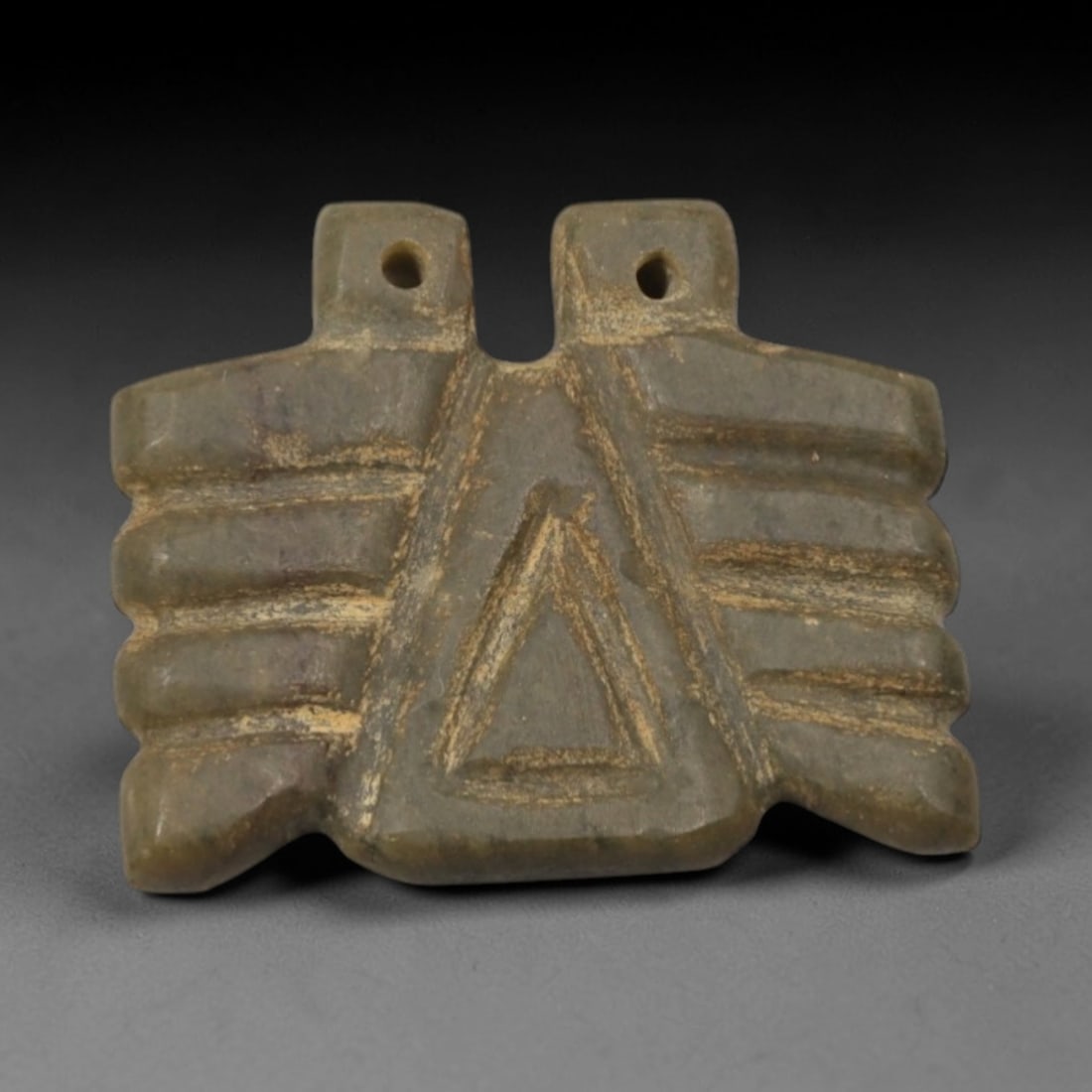 Ancient Green Stone Geometric Pendant - Near Eastern Ritual Amulet, 74XP: Carved from a muted, earthy green stone, this miniature pendant features a highly stylized geometric design, a distinctive motif in ancient Near Eastern ritual art. The symmetrical form is defined by