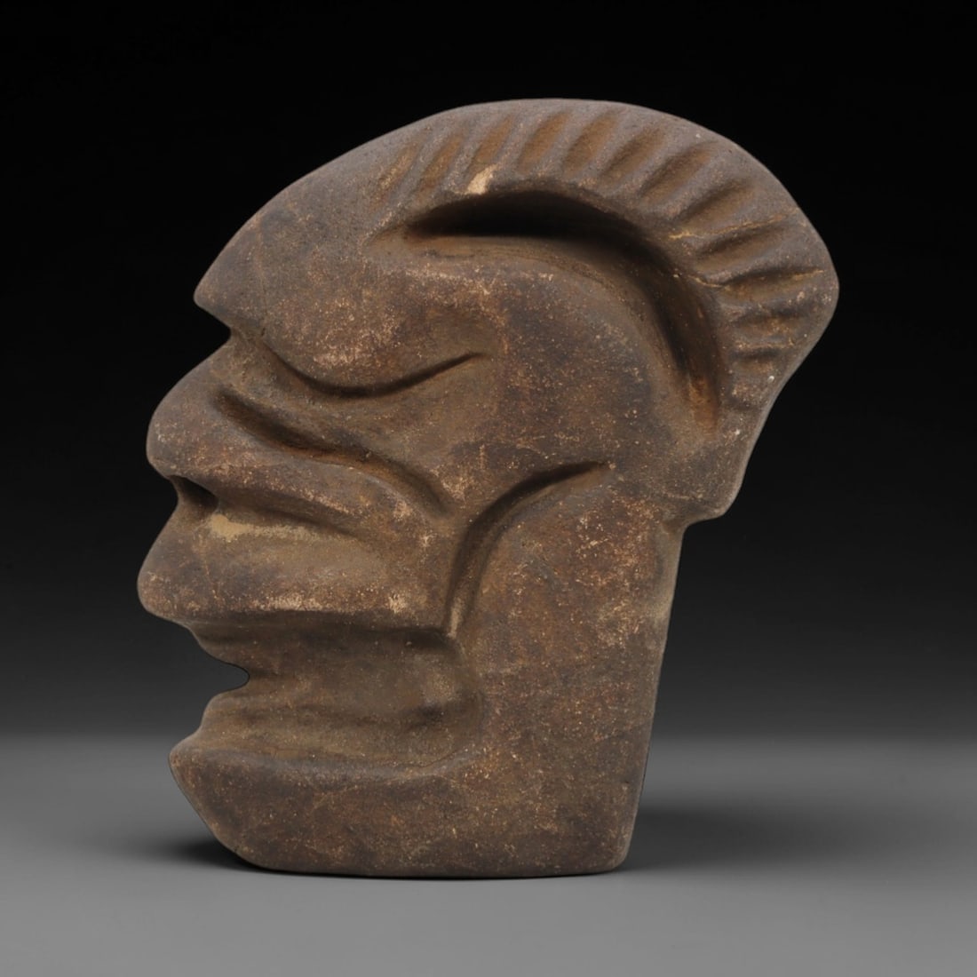 Ancient Stone Tribal Head - Ritual Figurine, 31FX: Carved from a dense, earthy-brown stone with a granular matrix, this artifact depicts a stylized tribal head in profile, featuring a prominent ridged crest, deeply incised facial lines, a pronounced n
