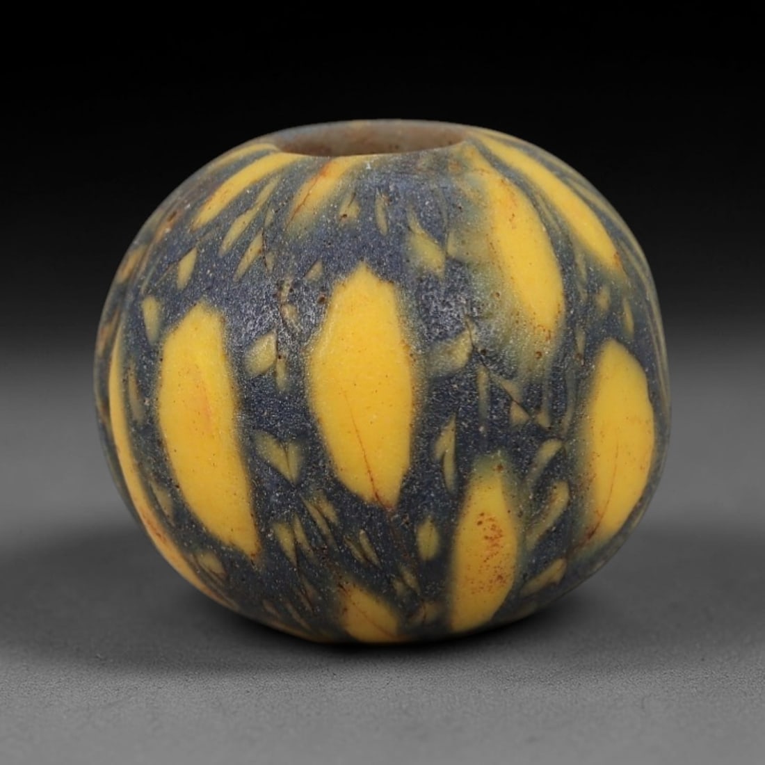 Ancient Glass Mosaic Bead - Islamic Amulet, 3FW: Crafted from opaque dark blue glass with bright yellow elongated inclusions, this spherical bead employs the mosaic glass technique, where colored glass canes are fused and sliced to form a repeating