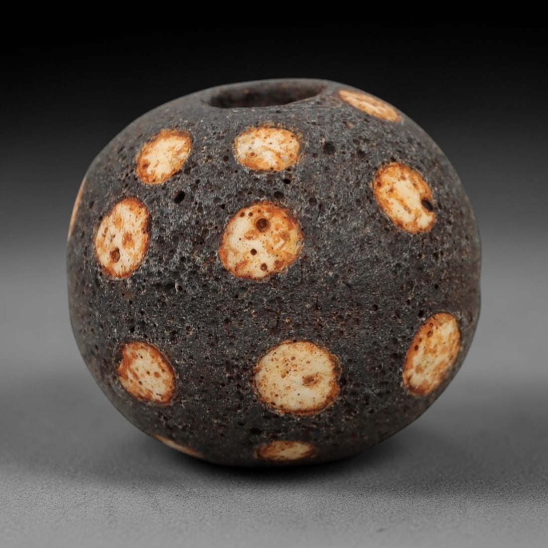 Ancient Glass Spotted Bead - Roman/Egyptian Amulet Bead, 54FW: This spherical bead is crafted from porous dark glass, adorned with evenly spaced circular white inlays edged with warm orange-brown patina, characteristic of Roman and Egyptian glassworking tradition