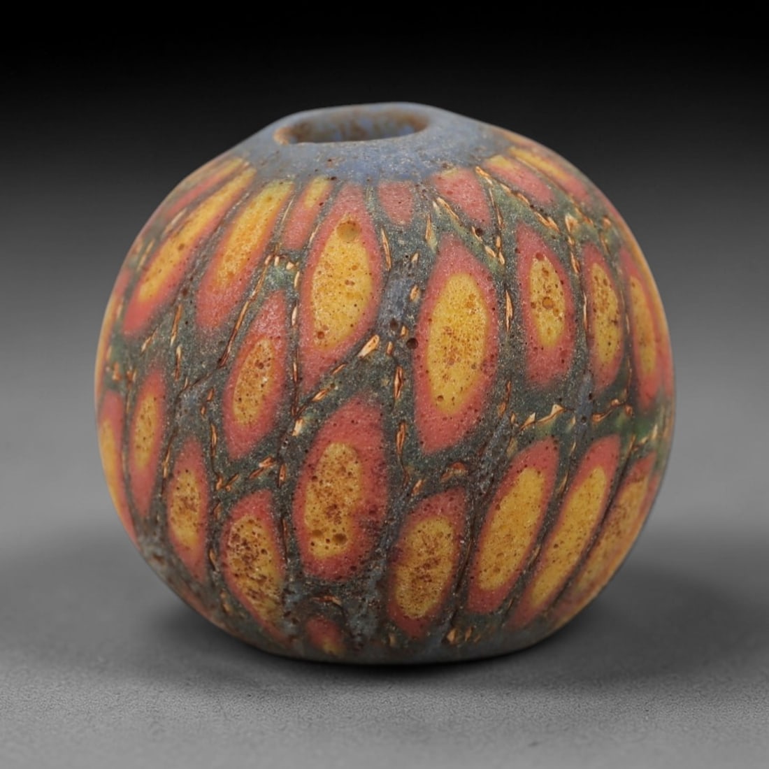 Ancient Glass Eye Bead - Roman Mosaic Amulet, 46FW: Crafted from translucent teal glass with opaque red and yellow inclusions, this spherical bead employs the mosaic glass technique, where colored glass canes are fused and sliced to form repeating eye-