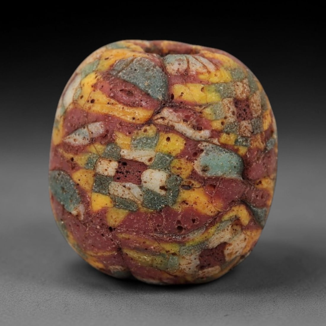 Ancient Islamic Glass Bead - Mosaic Patchwork Amulet Bead, 52FW: This spherical bead is crafted from layered mosaic glass, featuring a vibrant patchwork of red, yellow, teal, and cream segments, characteristic of medieval Islamic glassworking traditions. A central
