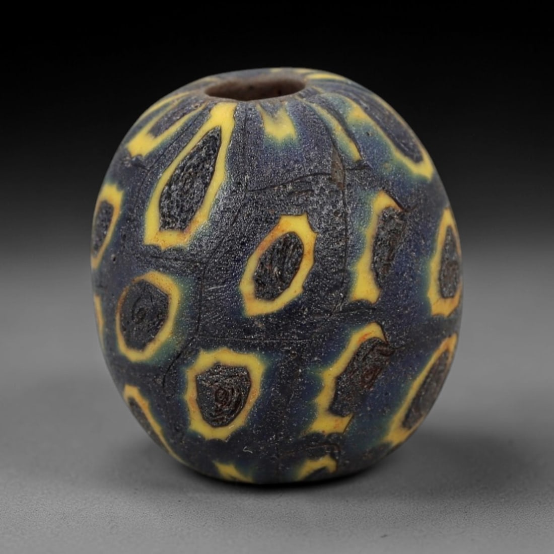 Ancient Viking Glass Bead - Eye Mosaic Amulet Bead, 60FW: This ovoid bead is crafted from deep indigo glass, adorned with repeating eye-shaped motifs outlined in bright yellow-each with a dark, spiraled center-characteristic of Viking Age glassworking tradit
