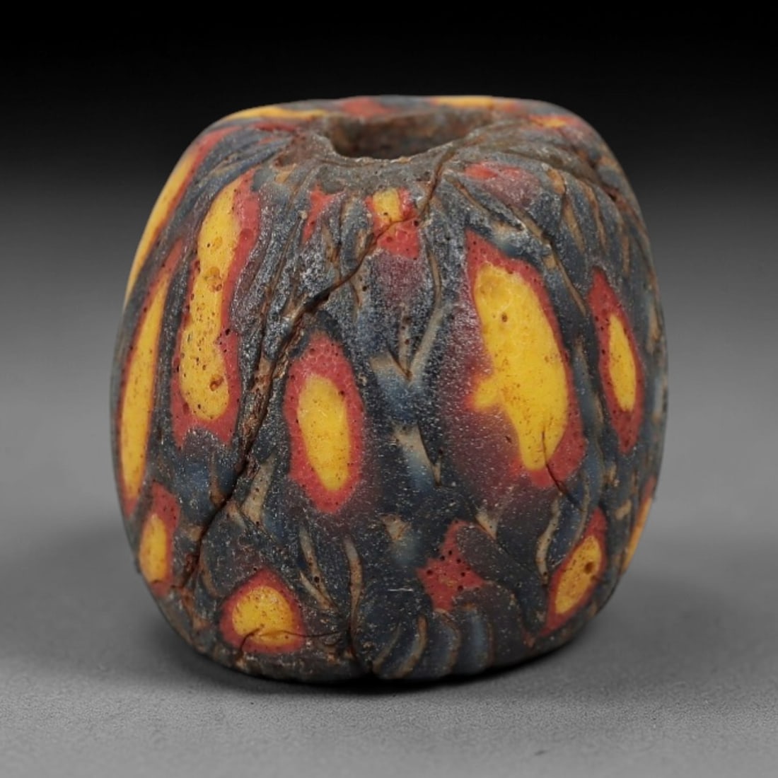Ancient Viking Glass Bead - Organic Mosaic Amulet Bead, 57FW: This barrel-shaped bead is crafted from layered marbled glass, featuring bold organic oval motifs in bright yellow and red against a deep indigo base-characteristic of Viking Age glassworking traditio