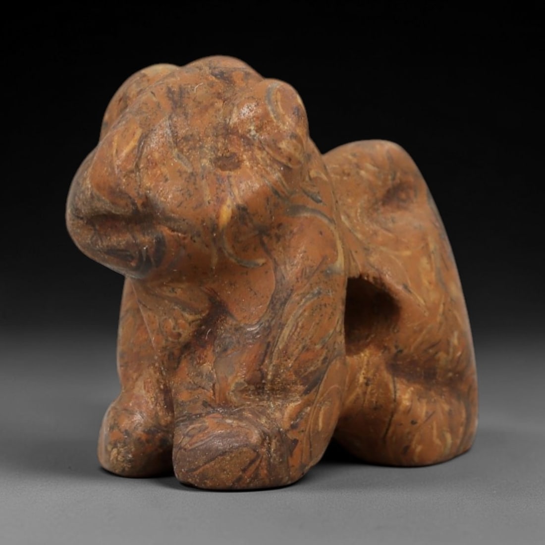 Ancient Marbled Stone Zoomorphic Amulet - Near Eastern Figurine, 96AD: Carved from striking orange and brown marbled stone, this amulet presents a compact, stylized zoomorphic form in a seated, upright posture. The creature is rendered with abstracted, rounded contours a