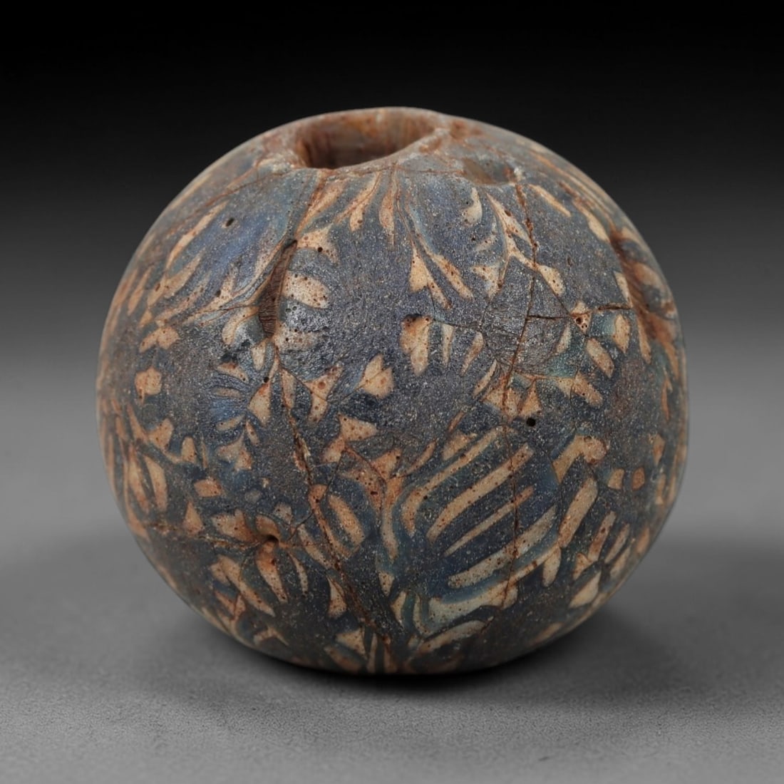 Ancient Glass Mosaic Bead - Roman/Egyptian Amulet Bead, 56FW: This spherical bead is crafted from layered mosaic glass, featuring a deep blue base overlaid with intricate white and tan linear patterns that form interwoven, organic motifs across the surface. A ce