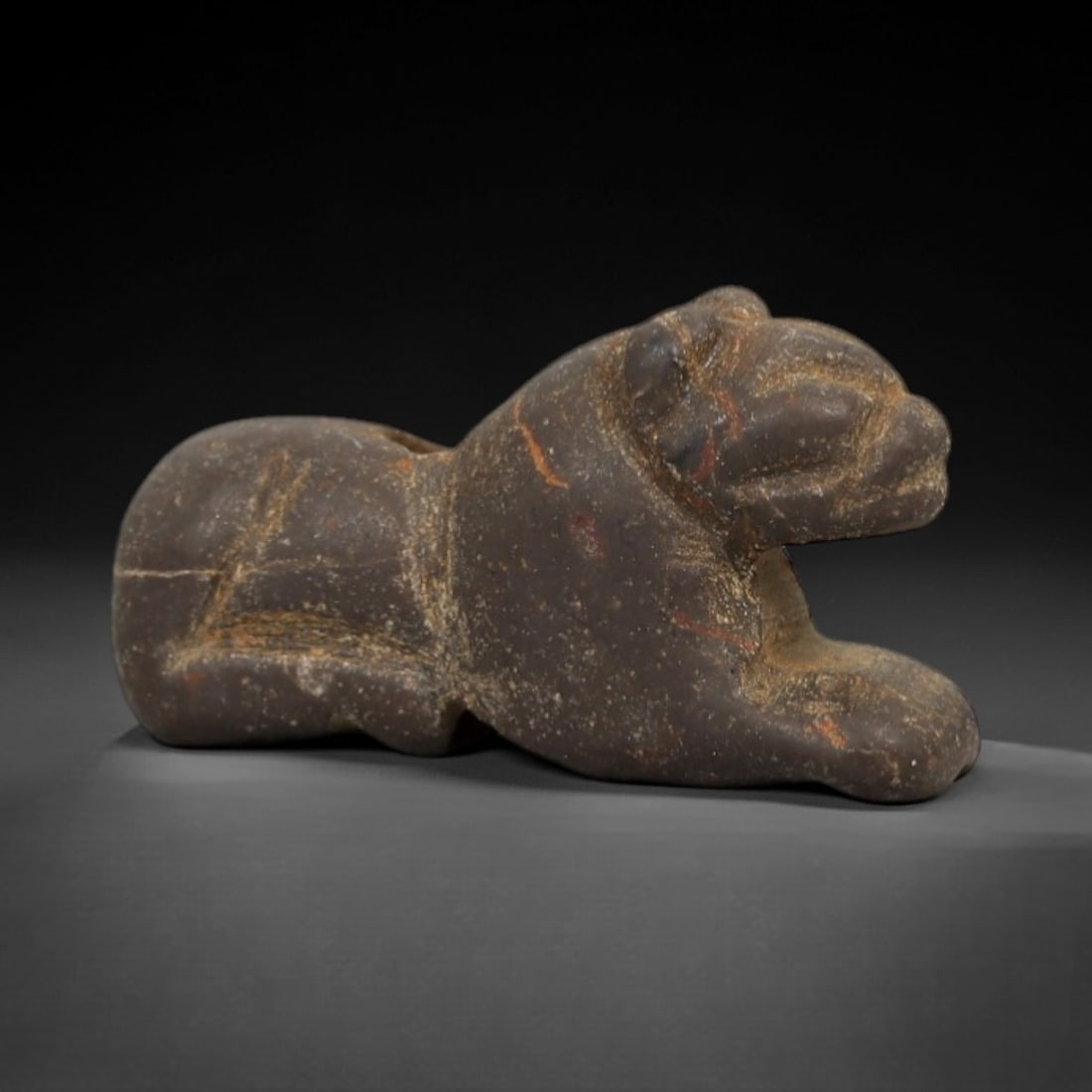 Ancient Dark Stone Recumbent Feline - Near Eastern Amulet, 8AE: Carved from dark speckled stone with faint mineral veins, this amulet depicts a recumbent feline in a compact, stylized form. The creature is rendered in a prone posture, with simplified facial featur
