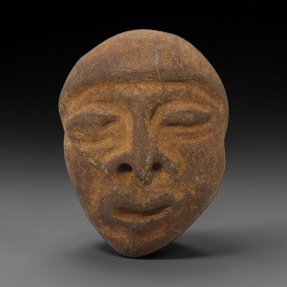 Ancient Stone Anthropomorphic Head - African Tribal Figurine, 66FW: Carved from a compact, earthy-brown stone, this artifact depicts a stylized anthropomorphic head with closed, incised eyes, a defined nasal bridge with double nostrils, and a subtle mouth, embodying t