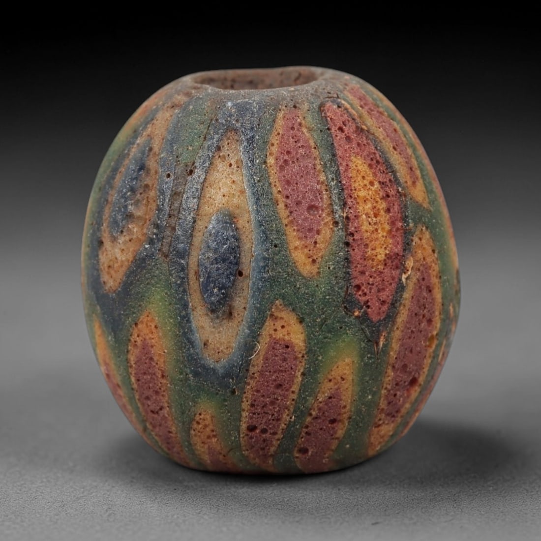 Ancient Islamic Glass Bead - Organic Mosaic Amulet Bead, 35FW: This spherical bead is crafted from porous layered glass, featuring repeating organic oval motifs in red, yellow, green, and deep blue, characteristic of medieval Islamic glassworking traditions. A ce