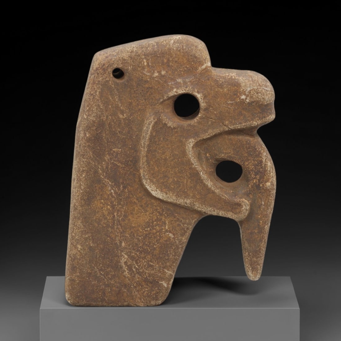 Ancient Stone Anthropomorphic Head - Tribal Ritual Amulet, 38FX: Carved from a dense, sandy-brown stone with a weathered, granular patina, this artifact depicts a stylized anthropomorphic head featuring bold, pierced circular eye sockets, a simplified nasal structu