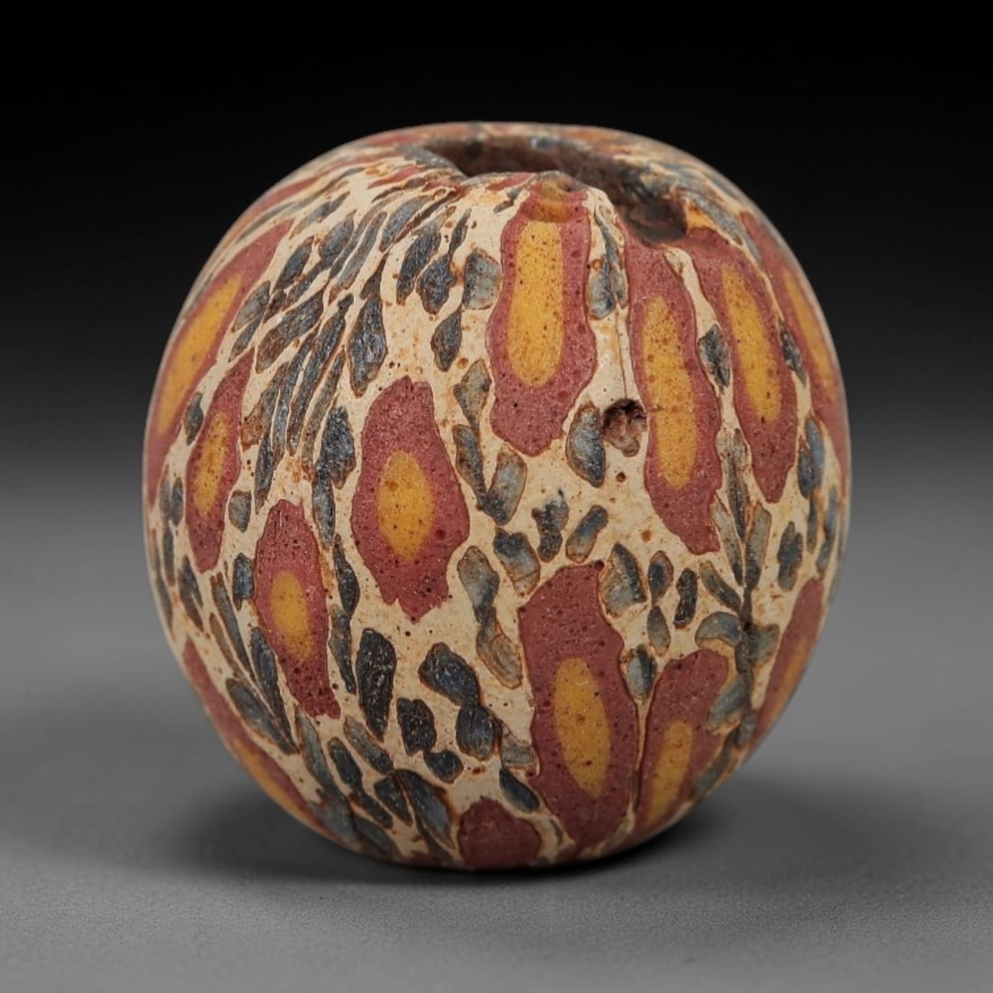 Ancient Islamic Glass Bead - Organic Mosaic Amulet Bead, 25FW: This spherical bead is crafted from layered mosaic glass, featuring repeating organic teardrop-shaped motifs with yellow centers, red outer rings, and intricate blue-and-cream matrix patterns, charact