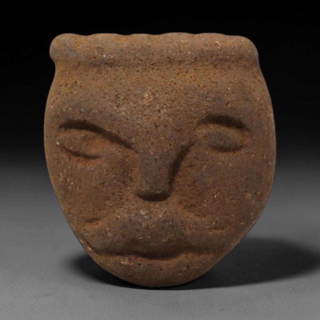 Ancient Stone Anthropomorphic Head - African Tribal Relic, 75FW: Carved from a coarse, earthy-brown stone with a granular texture, this artifact presents a compact anthropomorphic head featuring incised, low-relief eyes with subtle brow ridges, a pronounced nasal s