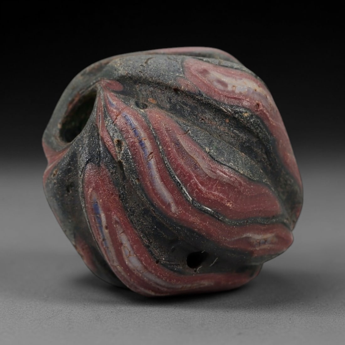 Ancient Islamic Glass Bead - Swirled Marbled Amulet Bead, 28FW: This faceted bead is crafted from layered marbled glass, featuring bold swirling stripes of deep red, white, and dark green with subtle blue accents, characteristic of medieval Islamic glassworking tr