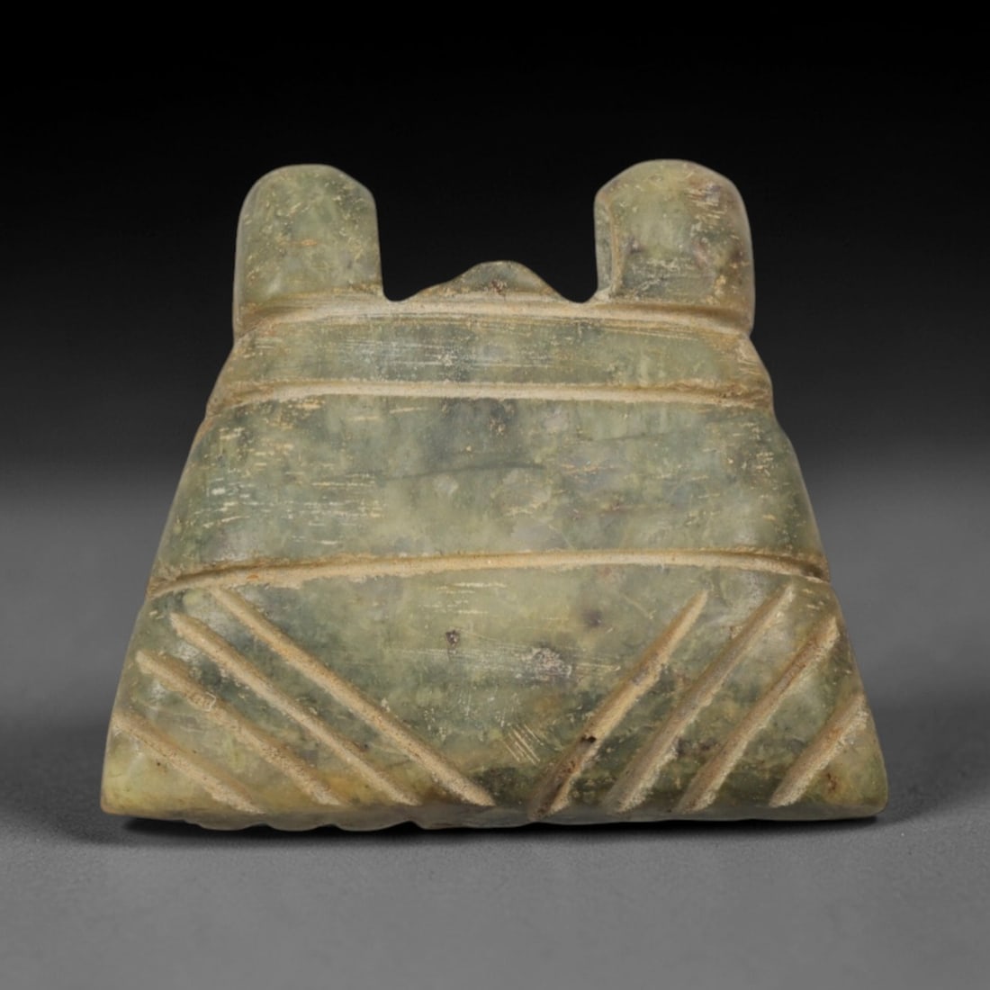 Ancient Green Stone Amulet - Near Eastern Twin-Horned Pendant, 57XP: Carved from a mottled green stone, this amulet features a trapezoidal form with two raised horn-like protrusions at the apex, a distinctive iconographic element in ancient Near Eastern ritual art. Hor