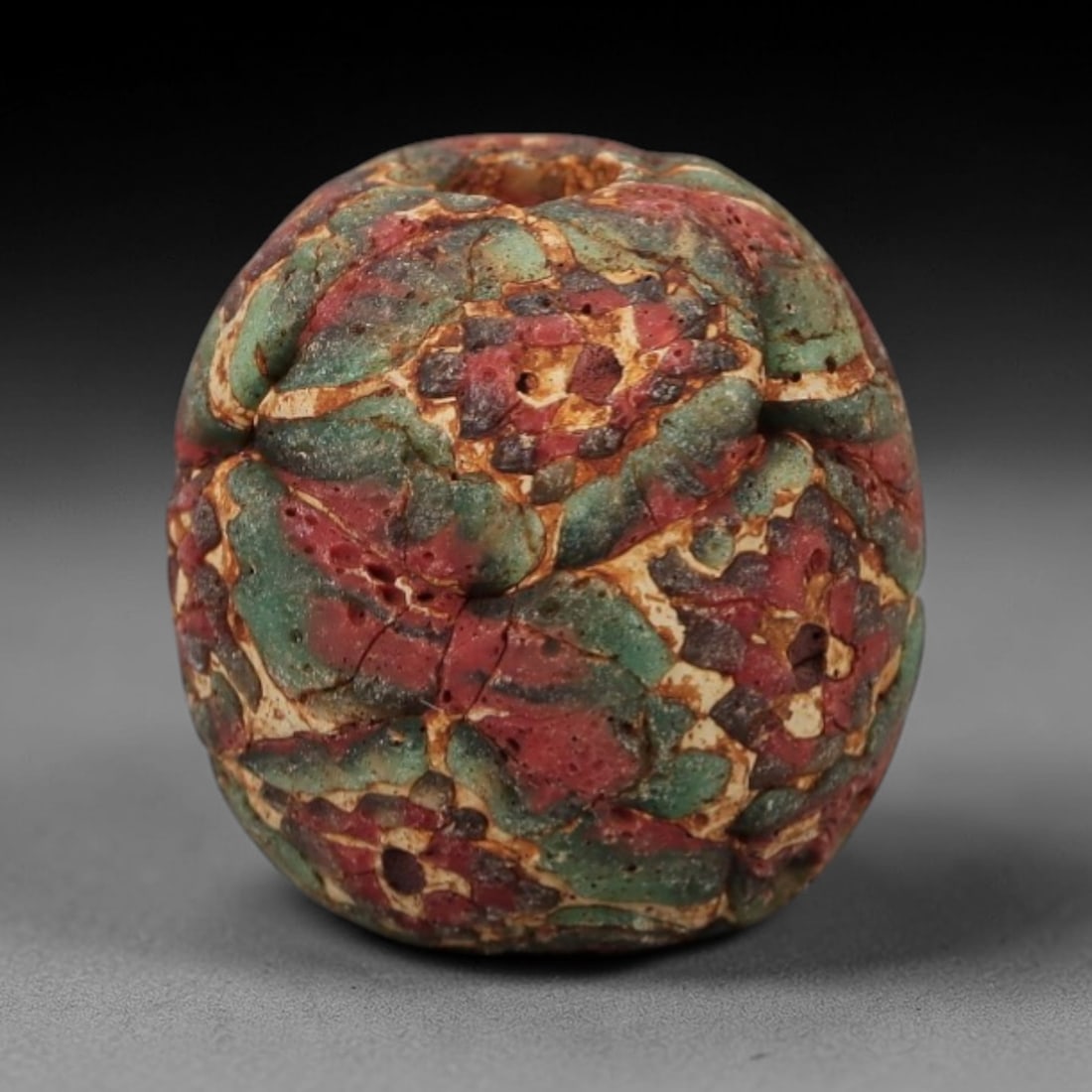 Ancient Islamic Glass Bead - Mosaic Patchwork Amulet Bead, 5FW: This spherical bead is crafted from layered mosaic glass, featuring a patchwork of red and green segments separated by cream-toned matrix lines, characteristic of medieval Islamic glassworking traditi