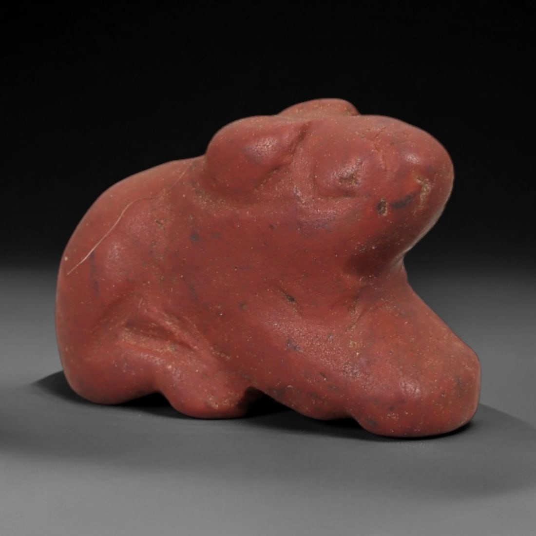 Ancient Red Stone Recumbent Zoomorphic Amulet - Near Eastern Relic, 7AE: Carved from rich red stone with natural granular texture, this amulet depicts a stylized recumbent zoomorphic form in a compact, rounded posture. The creature features simplified facial contours and s