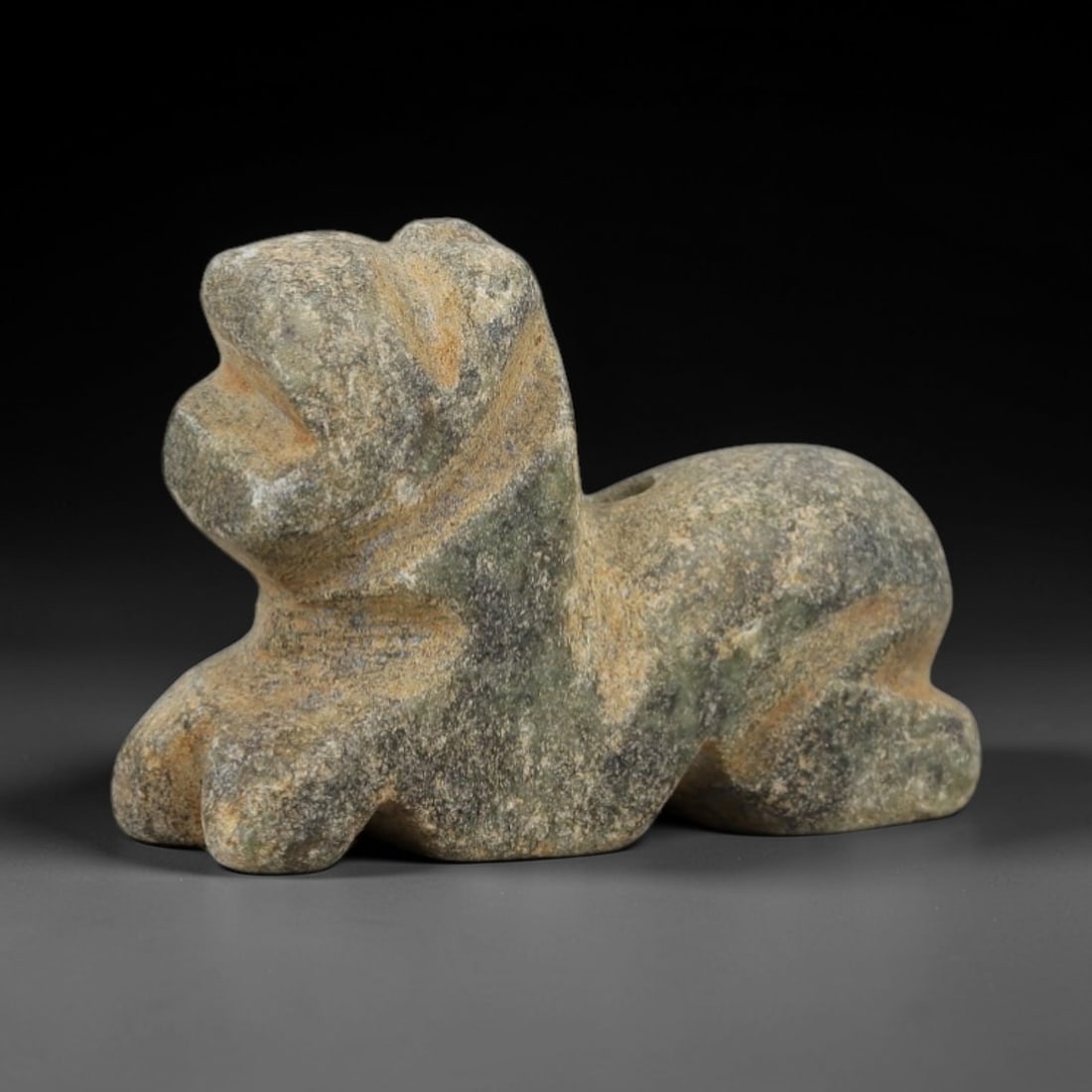 Ancient Mottled Stone Recumbent Feline - Near Eastern Amulet, 89AD: Carved from mottled greenish-gray stone with natural mineral speckling, this amulet depicts a recumbent feline in a compact, stylized form. The creature is rendered in a prone resting posture, with si