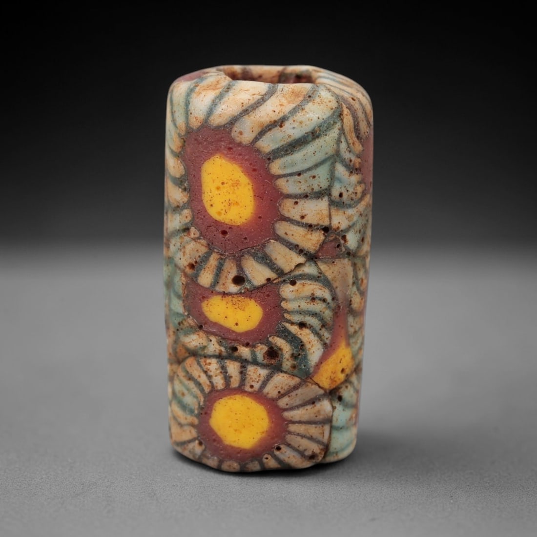 Ancient Islamic Glass Bead - Floral Mosaic Cylinder Bead, 29FW: This cylindrical bead is crafted from layered mosaic glass, featuring repeating floral motifs with yellow centers, red inner rings, and teal-and-white petal-like linear patterns, characteristic of med