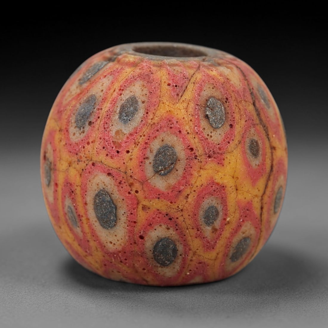 Ancient Glass Eye Bead - Roman/Egyptian Mosaic Amulet Bead, 38FW: This spherical bead is crafted from layered mosaic glass, featuring a warm yellow base overlaid with repeating concentric eye-shaped motifs in red, white, and dark grey, evoking the protective "eye" a