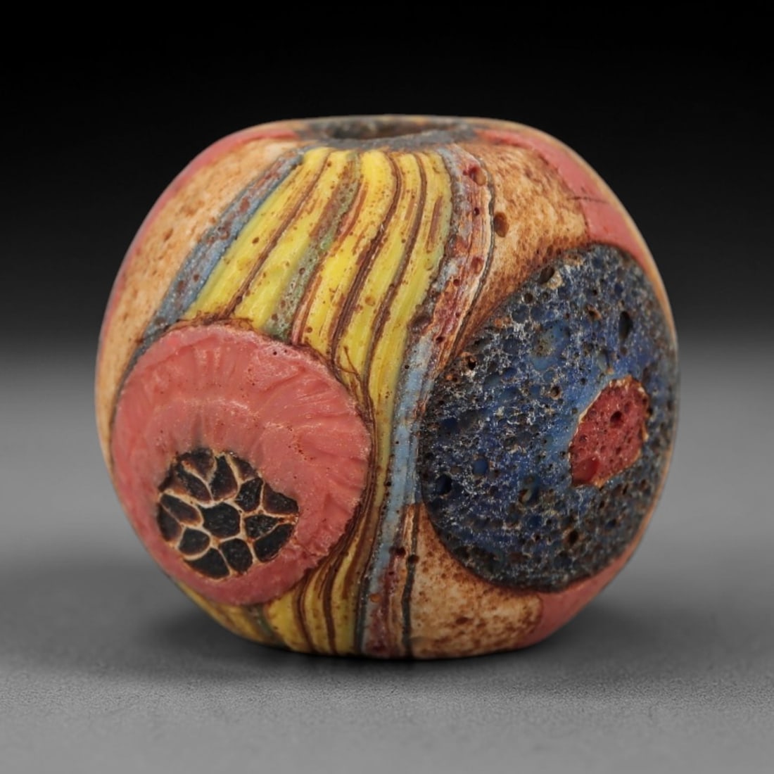 Ancient Glass Mosaic Bead - Islamic Amulet, 7FW, 7FW: Crafted from fused multicolored glass canes, this barrel-shaped bead features vertical yellow, blue, and red striations alongside two prominent circular mosaic inclusions. One inclusion displays a pin
