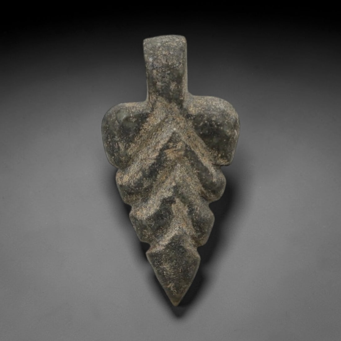 Ancient Stone Leaf Amulet - Near Eastern Carved Pendant, 31AG: This amulet is carved from a dark green stone with a granular texture and weathered, earthy patina. The form is a stylized leaf, with a rectangular upper suspension segment and a tapering lower body d