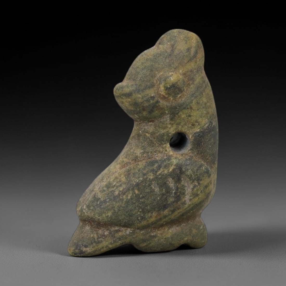 Ancient Stone Bird Amulet - Near Eastern Ritual Figurine, 28AG: This amulet is carved from a single piece of banded green stone, exhibiting a striated texture with earthy yellow and grey veining across its surface. The form is stylized as a seated bird, with a rou