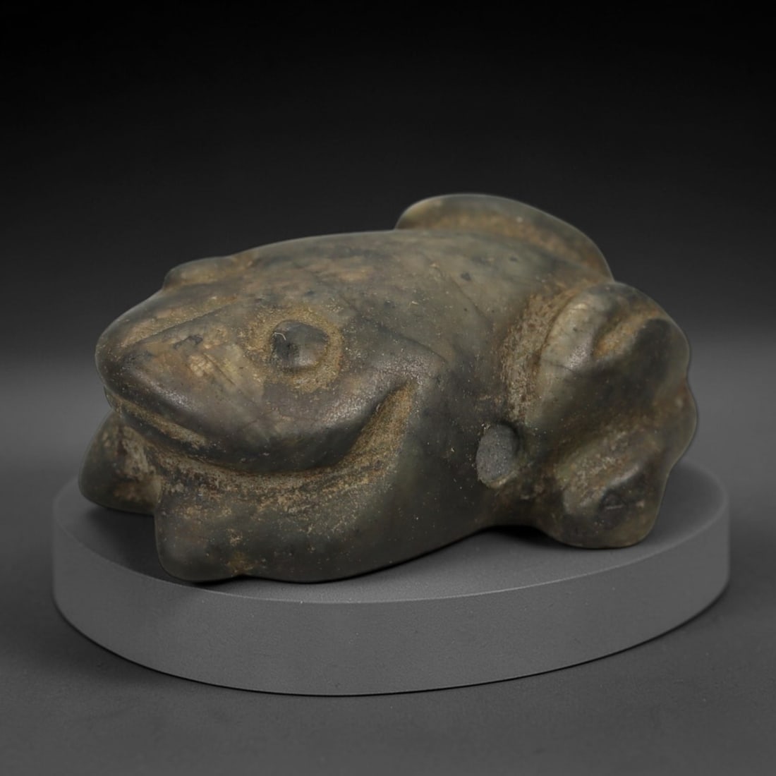 Ancient Stone Frog Amulet - Near Eastern Ritual Figurine, 51AE: This amulet is carved from a single piece of mottled grey-green stone, exhibiting a granular texture with subtle ochre patina and natural mineral veining across its surface. The form is stylized as a
