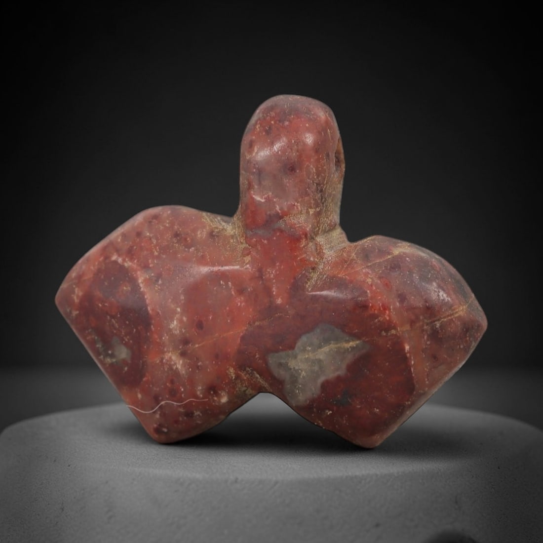Ancient Stone Bird Amulet - Near Eastern Ritual Figurine, 48AG: This amulet is carved from a single piece of mottled red stone, exhibiting a granular texture with pale grey inclusions and natural veining across its surface. The form is schematically rendered as a