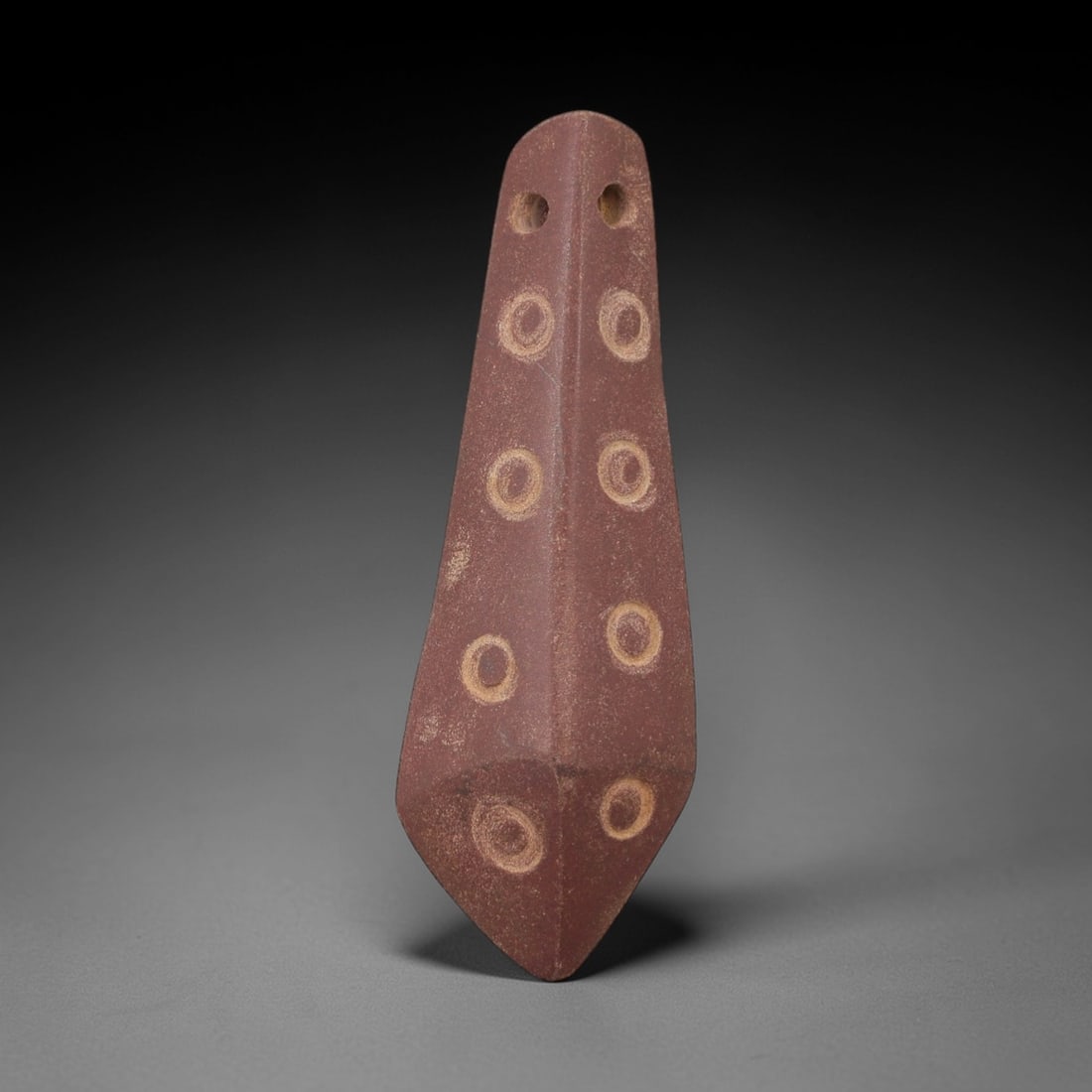 Ancient Egyptian Stone Amulet - Geometric Carved Figurine, 38AE: Carved from dark stone, this ancient Egyptian amulet exhibits a streamlined elongated form with evenly spaced circular incisions along its length, a motif characteristic of Egyptian apotropaic amulets