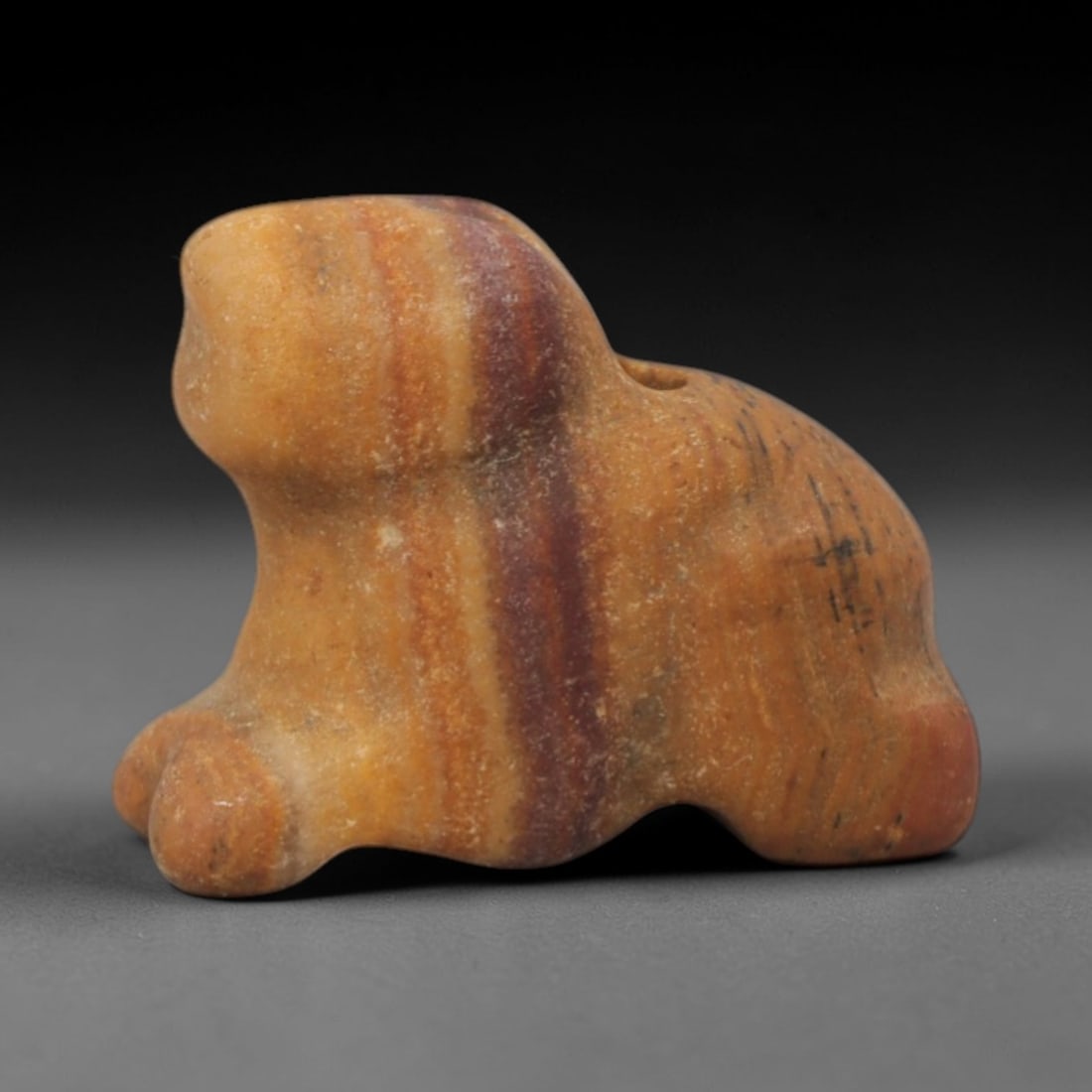 Ancient Stone Feline Amulet - Near Eastern Pendant, 27XQ: Carved from a banded yellowish-brown stone with prominent reddish striations, this amulet depicts a stylized recumbent feline, with a rounded head, compact body, and short sturdy limbs. A small suspen